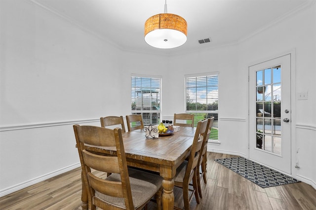 dining room featuring baseboards, ornamental molding, wood finished floors, and visible vents
