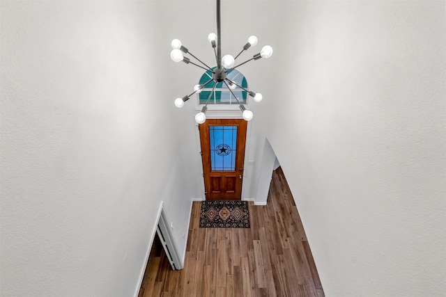 foyer entrance featuring baseboards, a notable chandelier, wood finished floors, and a high ceiling