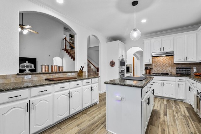 kitchen with a ceiling fan, backsplash, arched walkways, under cabinet range hood, and white cabinetry