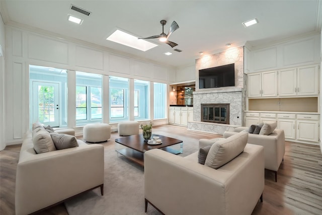 living room with light hardwood / wood-style floors, a stone fireplace, ceiling fan, and ornamental molding