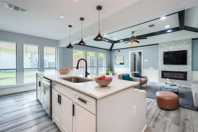 kitchen with dishwasher, a stone fireplace, sink, hanging light fixtures, and white cabinetry