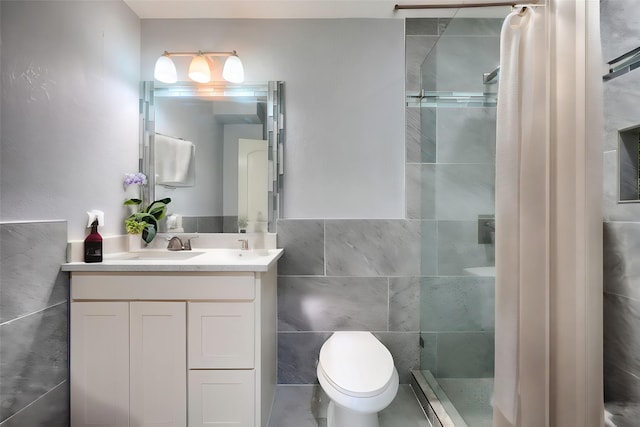 bathroom featuring vanity, toilet, tiled shower, and tile walls