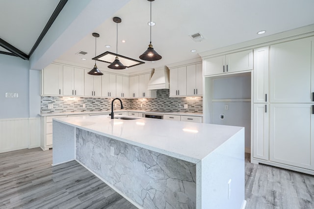 kitchen featuring white cabinets, a center island with sink, sink, light stone countertops, and custom range hood