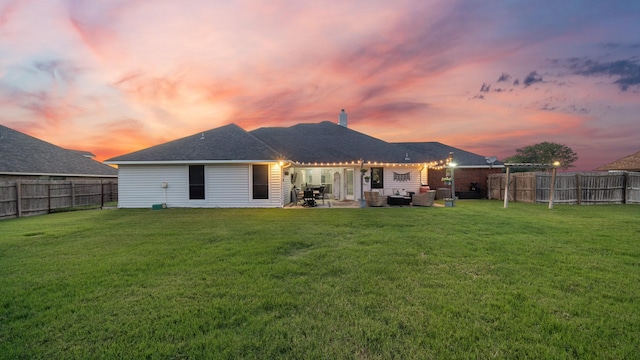 back house at dusk featuring a patio area and a lawn