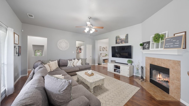 living room with dark hardwood / wood-style floors, ceiling fan, and a tiled fireplace