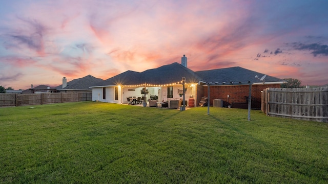 back house at dusk featuring outdoor lounge area, cooling unit, and a yard