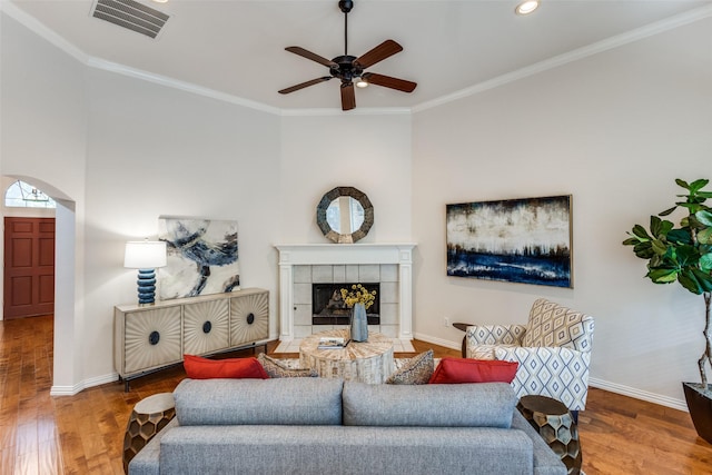 living room featuring a tile fireplace, wood-type flooring, ceiling fan, and crown molding