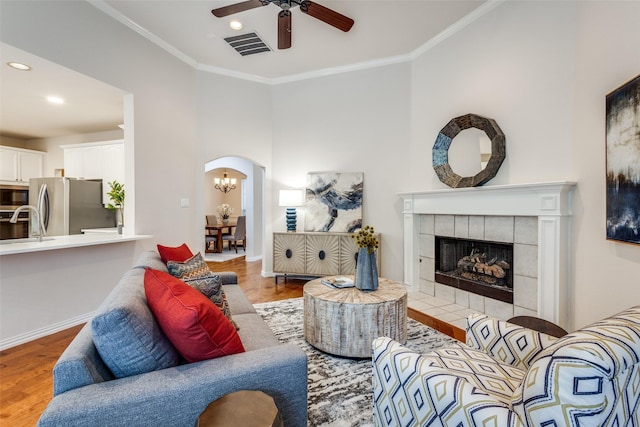 living room with crown molding, wood-type flooring, ceiling fan, and a fireplace