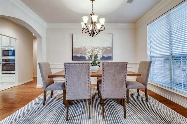 dining space with an inviting chandelier, ornamental molding, and hardwood / wood-style floors