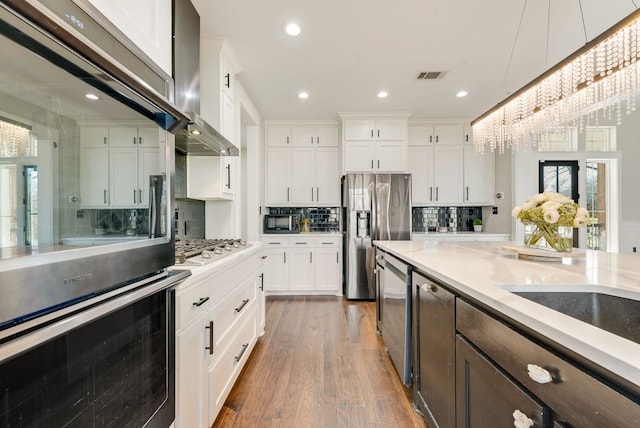 kitchen with appliances with stainless steel finishes, white cabinetry, dark hardwood / wood-style floors, a notable chandelier, and wall chimney exhaust hood