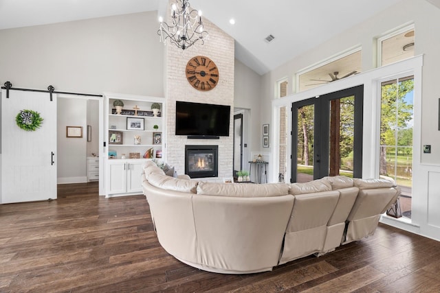 living room with high vaulted ceiling, a fireplace, a notable chandelier, a barn door, and dark wood-type flooring