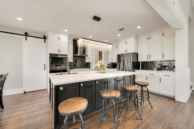 kitchen featuring pendant lighting, stainless steel fridge, an island with sink, white cabinets, and a barn door