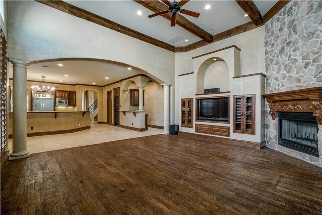 unfurnished living room featuring a stone fireplace, light hardwood / wood-style flooring, beamed ceiling, a towering ceiling, and ceiling fan with notable chandelier