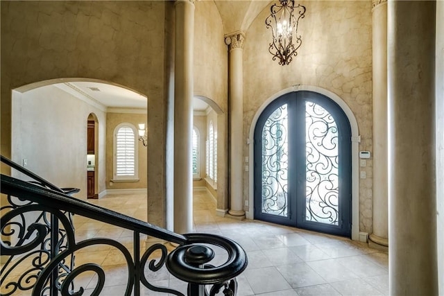 tiled foyer with french doors, a notable chandelier, ornamental molding, and a high ceiling