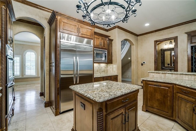 kitchen with pendant lighting, a center island, backsplash, crown molding, and built in appliances