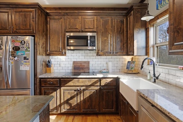 kitchen featuring sink, stainless steel appliances, light stone counters, decorative light fixtures, and light wood-type flooring