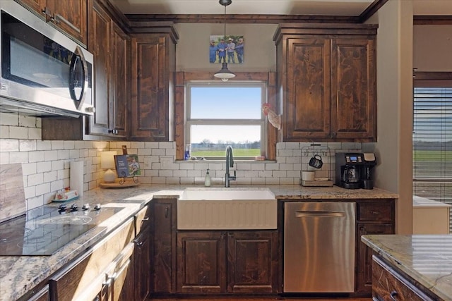 kitchen featuring stainless steel appliances, sink, light stone counters, and dark brown cabinetry