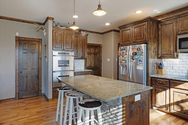 kitchen with stainless steel appliances, a kitchen island, pendant lighting, and light stone counters