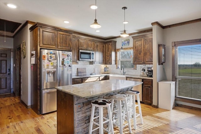 kitchen featuring pendant lighting, backsplash, stainless steel appliances, a center island, and light stone counters