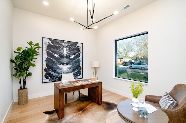 home office with an inviting chandelier and light hardwood / wood-style flooring