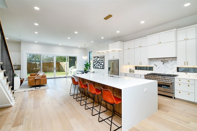 kitchen with high end appliances, a kitchen breakfast bar, a spacious island, hanging light fixtures, and white cabinetry