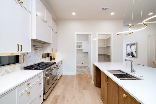 kitchen featuring white cabinetry, sink, light hardwood / wood-style flooring, decorative light fixtures, and range with two ovens