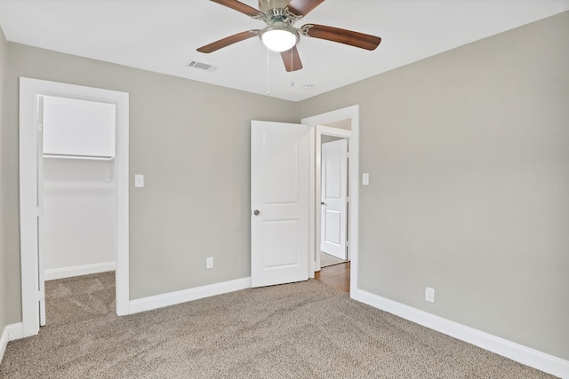 unfurnished bedroom with a walk in closet, a closet, ceiling fan, and carpet floors