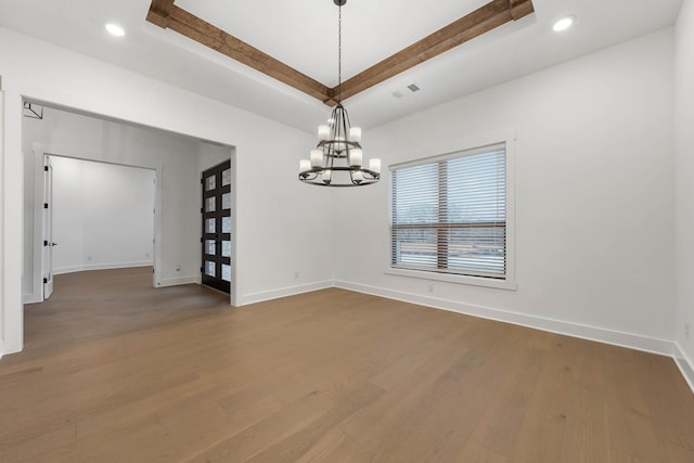 spare room with hardwood / wood-style floors, an inviting chandelier, and a raised ceiling