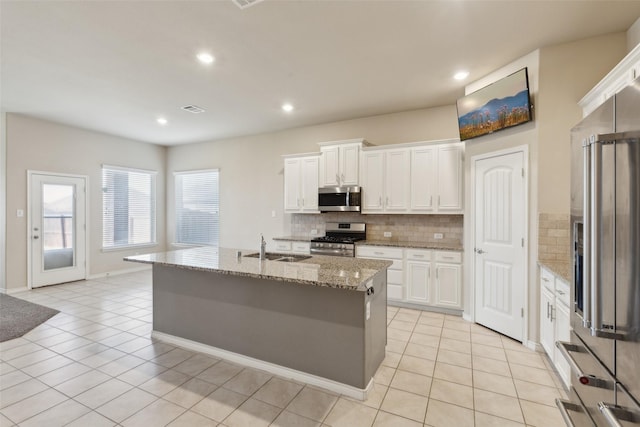 kitchen featuring backsplash, an island with sink, appliances with stainless steel finishes, light stone counters, and white cabinetry