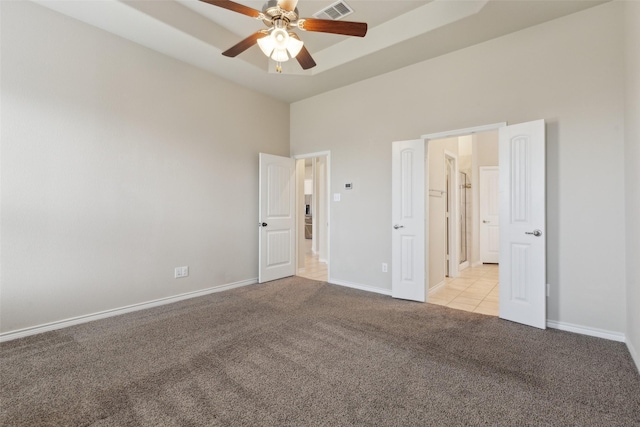 unfurnished bedroom featuring a high ceiling, light colored carpet, a raised ceiling, and ceiling fan