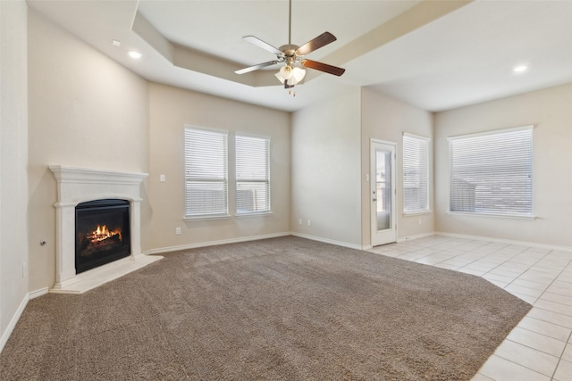 unfurnished living room with light tile patterned floors, a tray ceiling, and ceiling fan