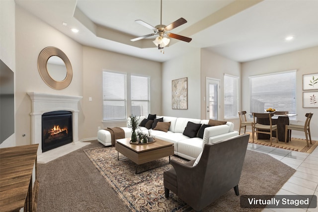 living room with a raised ceiling, ceiling fan, and light tile patterned flooring