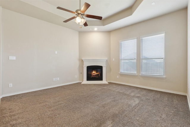 unfurnished living room with carpet floors, a tray ceiling, and ceiling fan