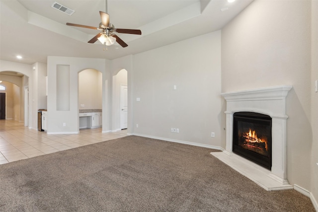 unfurnished living room with a raised ceiling, ceiling fan, and light colored carpet