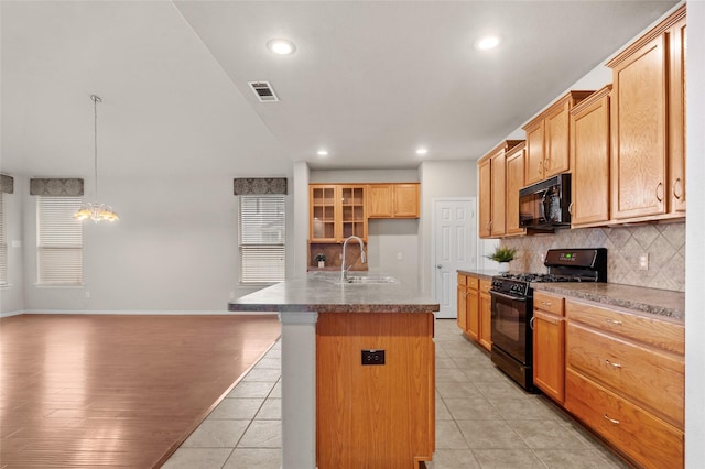 kitchen with sink, tasteful backsplash, an island with sink, decorative light fixtures, and black appliances