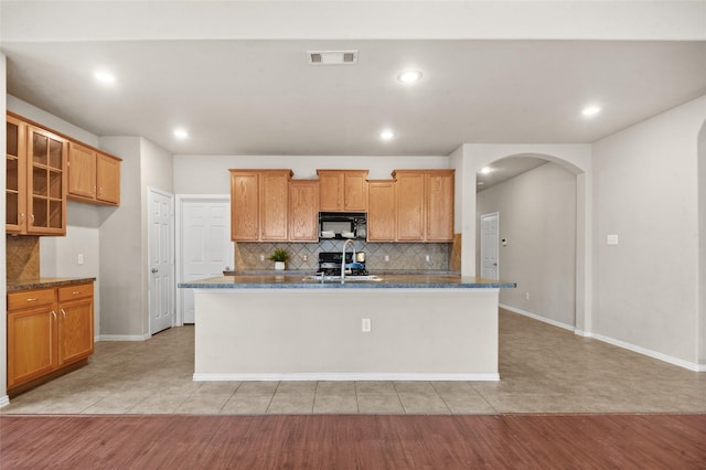 kitchen featuring sink, light tile patterned floors, a kitchen island with sink, and dark stone counters