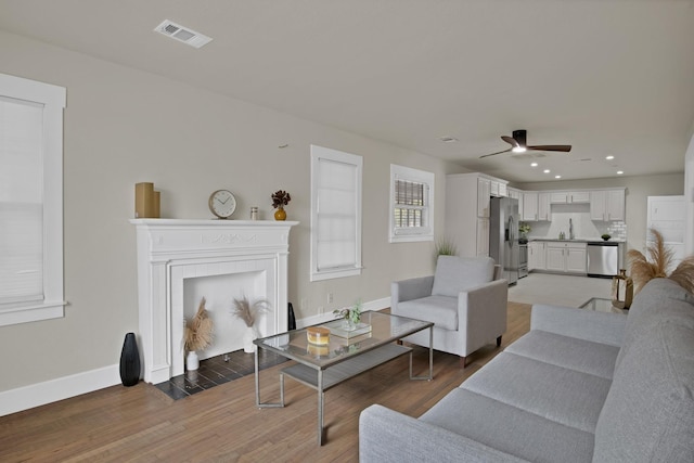 living room with baseboards, visible vents, light wood-style flooring, a fireplace with flush hearth, and recessed lighting