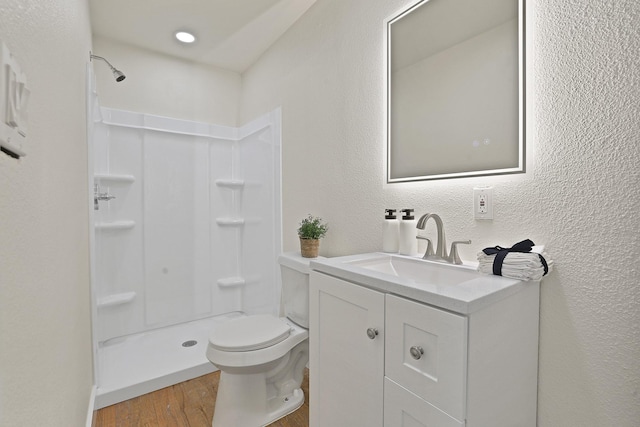 bathroom featuring toilet, a stall shower, wood finished floors, vanity, and a textured wall