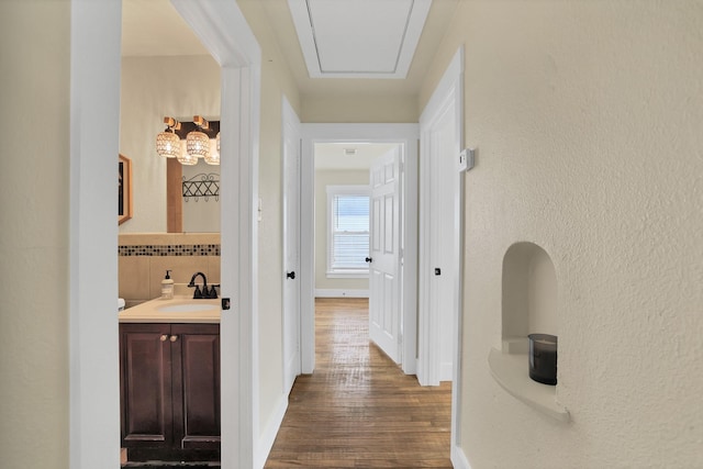 hall featuring a sink, baseboards, attic access, and dark wood-style floors