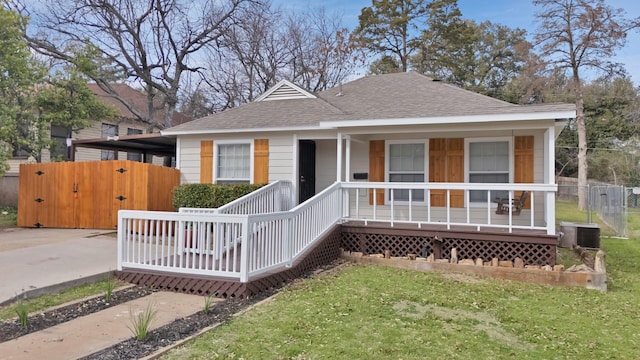 bungalow-style house featuring a front lawn, fence, roof with shingles, covered porch, and central AC unit