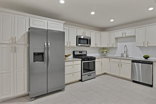 kitchen featuring light stone counters, decorative backsplash, appliances with stainless steel finishes, white cabinets, and a sink