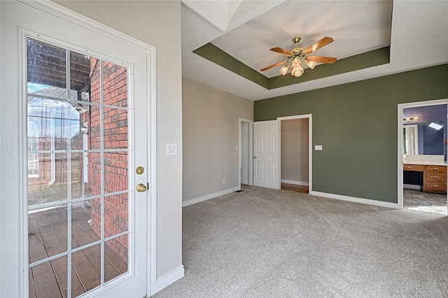 interior space with a tray ceiling, ceiling fan, light colored carpet, and ensuite bathroom