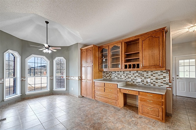 kitchen featuring tasteful backsplash, ceiling fan, built in desk, and a textured ceiling