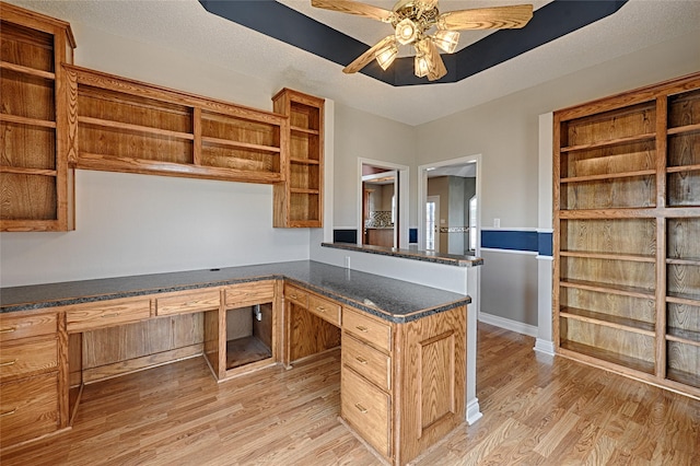 kitchen with kitchen peninsula, a textured ceiling, ceiling fan, built in desk, and light hardwood / wood-style flooring