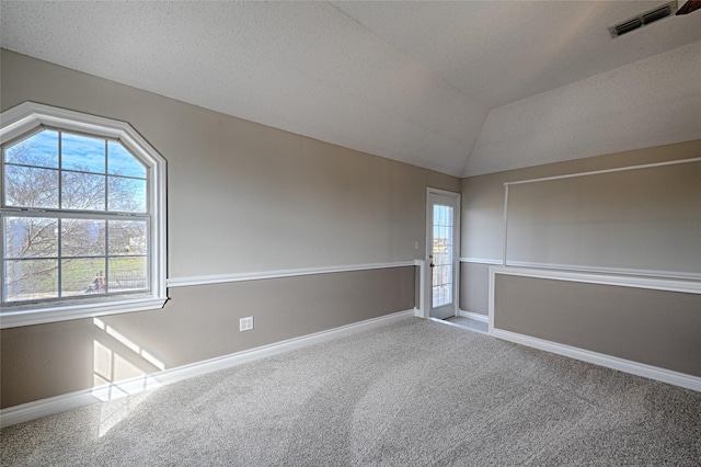 spare room with a textured ceiling, carpet floors, and vaulted ceiling