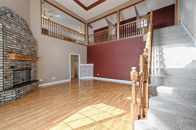 unfurnished living room with hardwood / wood-style flooring, ceiling fan, a towering ceiling, and a brick fireplace