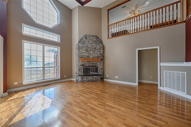 unfurnished living room featuring ceiling fan, a fireplace, a high ceiling, and light hardwood / wood-style flooring