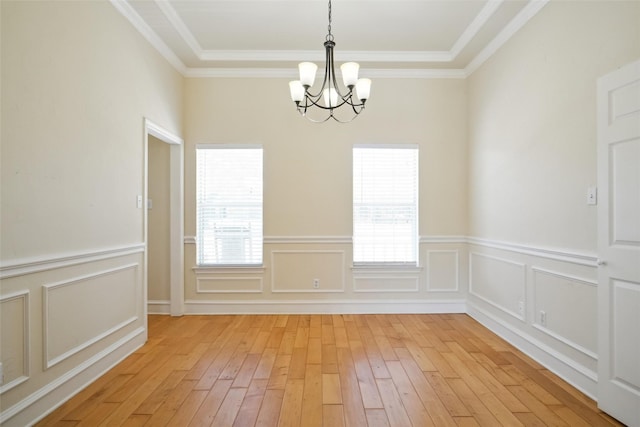 unfurnished dining area featuring light wood-type flooring, a chandelier, a decorative wall, and ornamental molding