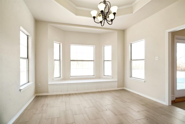 empty room with light wood-type flooring, plenty of natural light, a tray ceiling, and a notable chandelier