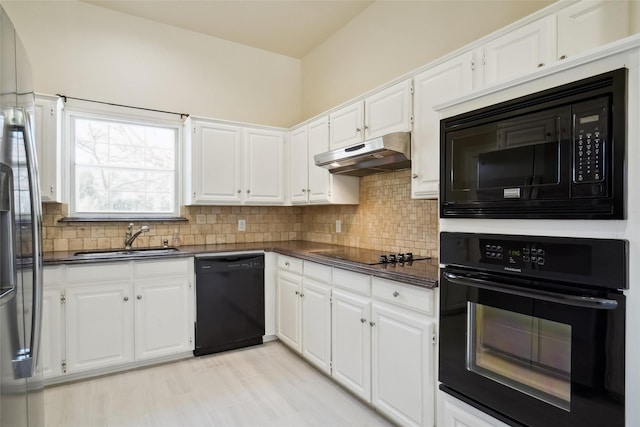 kitchen with dark countertops, white cabinetry, a sink, under cabinet range hood, and black appliances